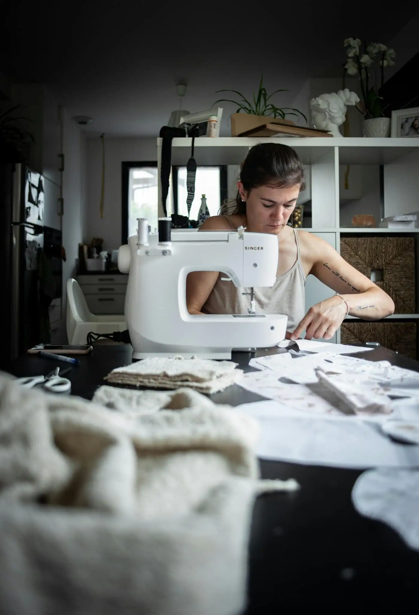 Putri Hanis, stylist, working at a sewing machine at a table covered in fabric and patterns